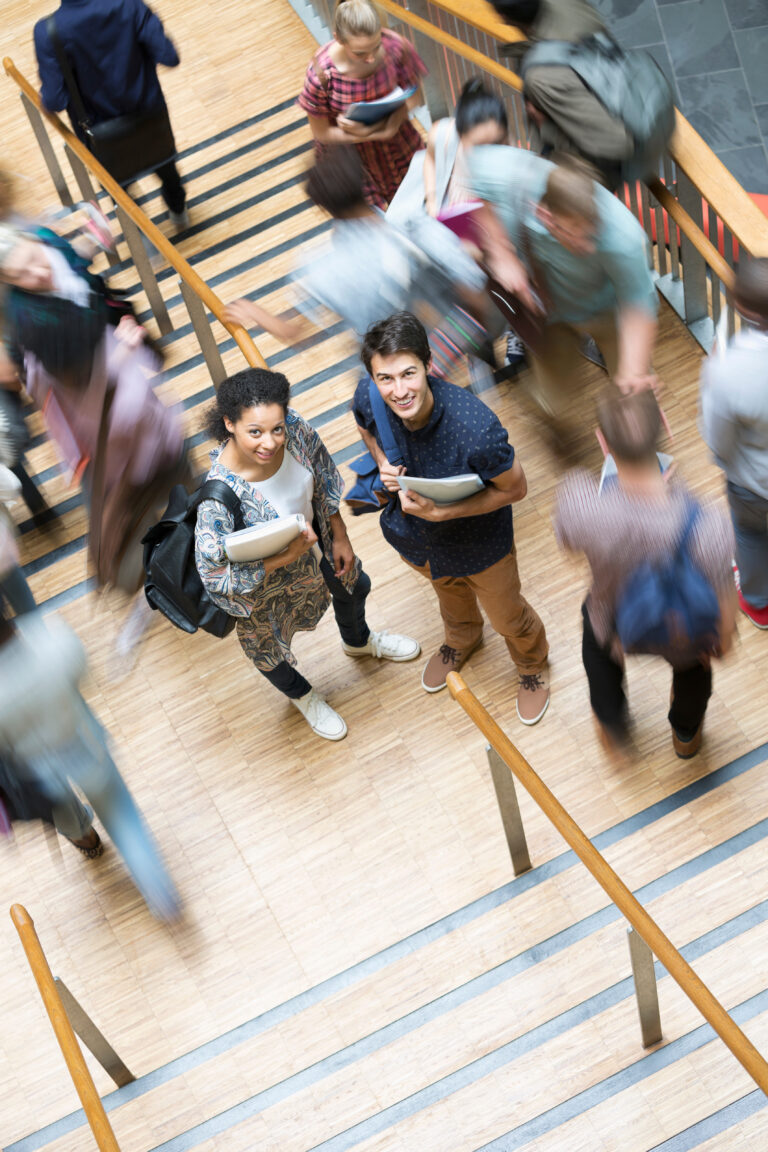 Elevated view of two smiling students standing on stairs other students going up down